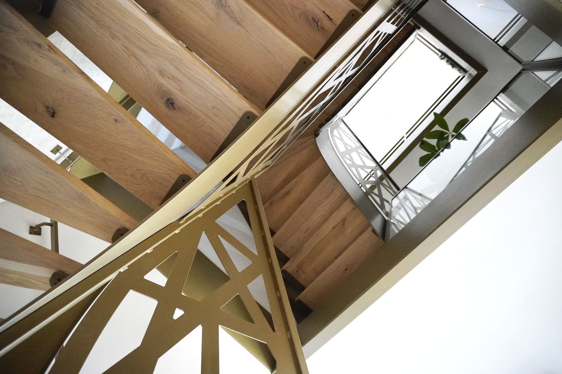 Houten trap met gouden leuning, van onderaf gezien. Licht stroomt van boven naar beneden.