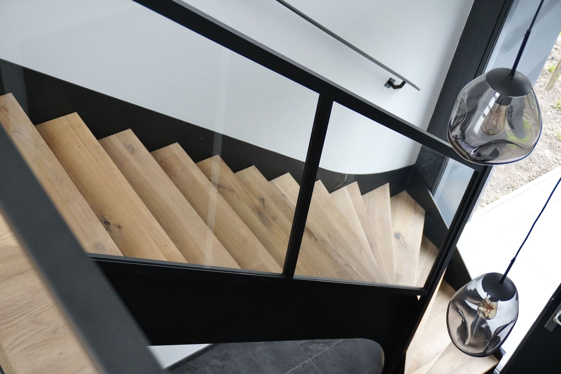 Houten trap met zwarte leuning en moderne verlichting.
