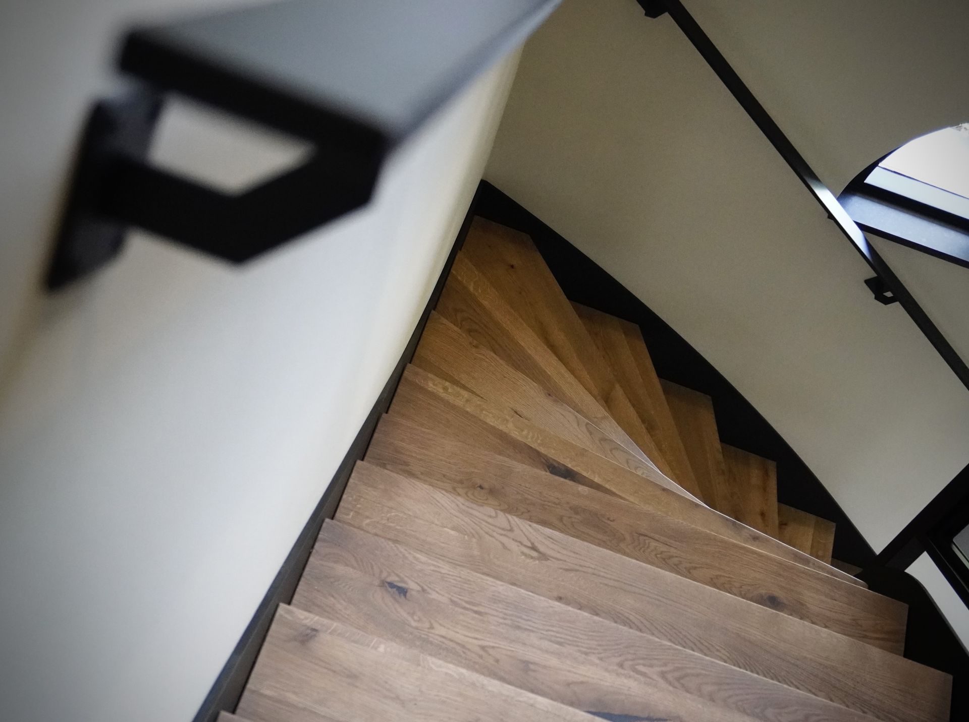 Houten wenteltrap met zwarte leuning en witte muur.