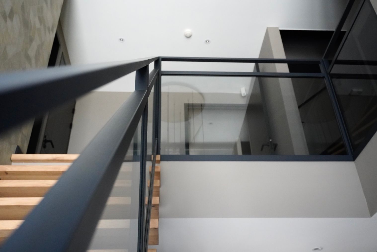 Trap met houten treden en zwarte leuning, glazen afscheiding naar de bovenverdieping, moderne architectuur.