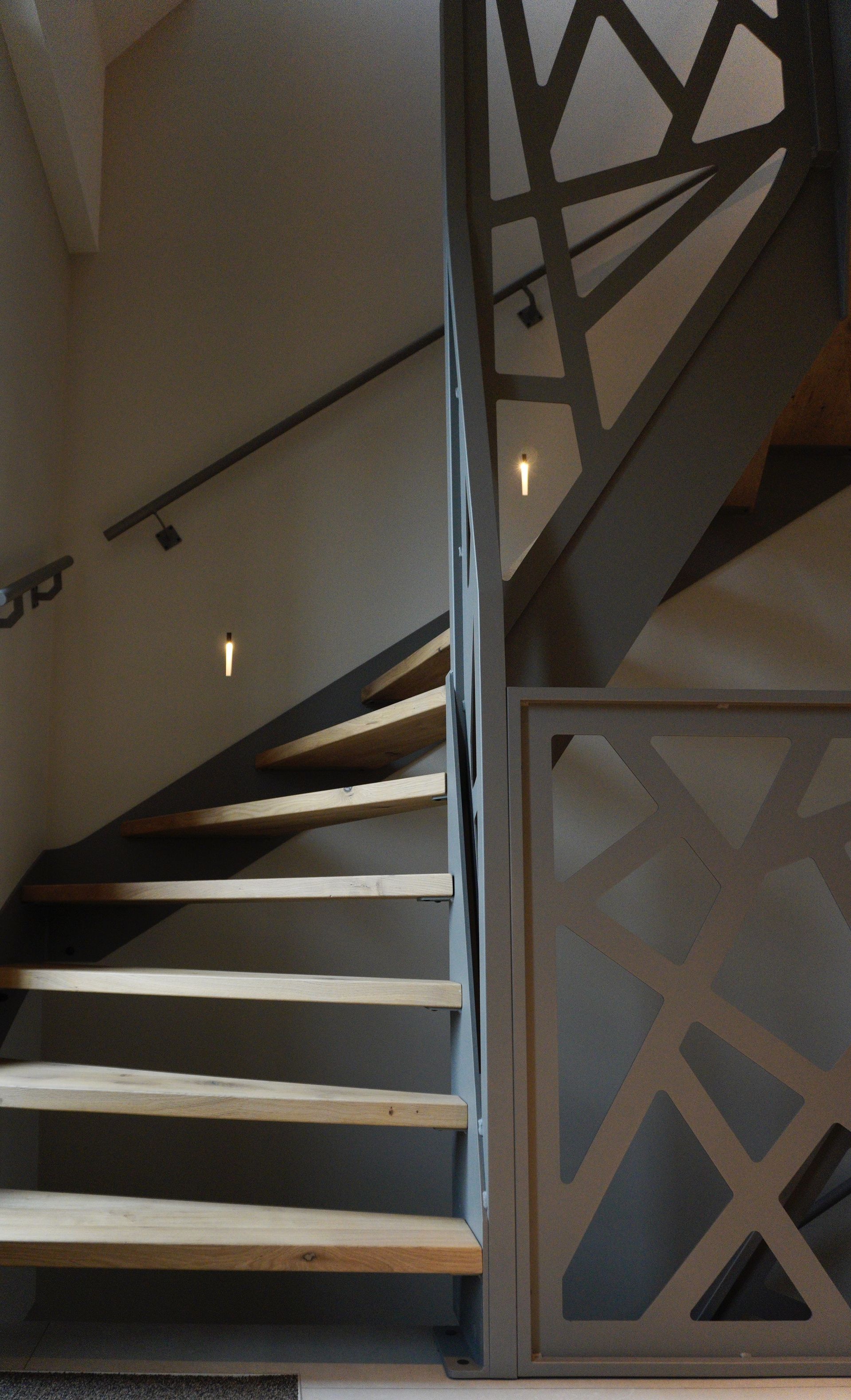 Houten trap met geometrische grijze metalen leuning en inbouwverlichting.