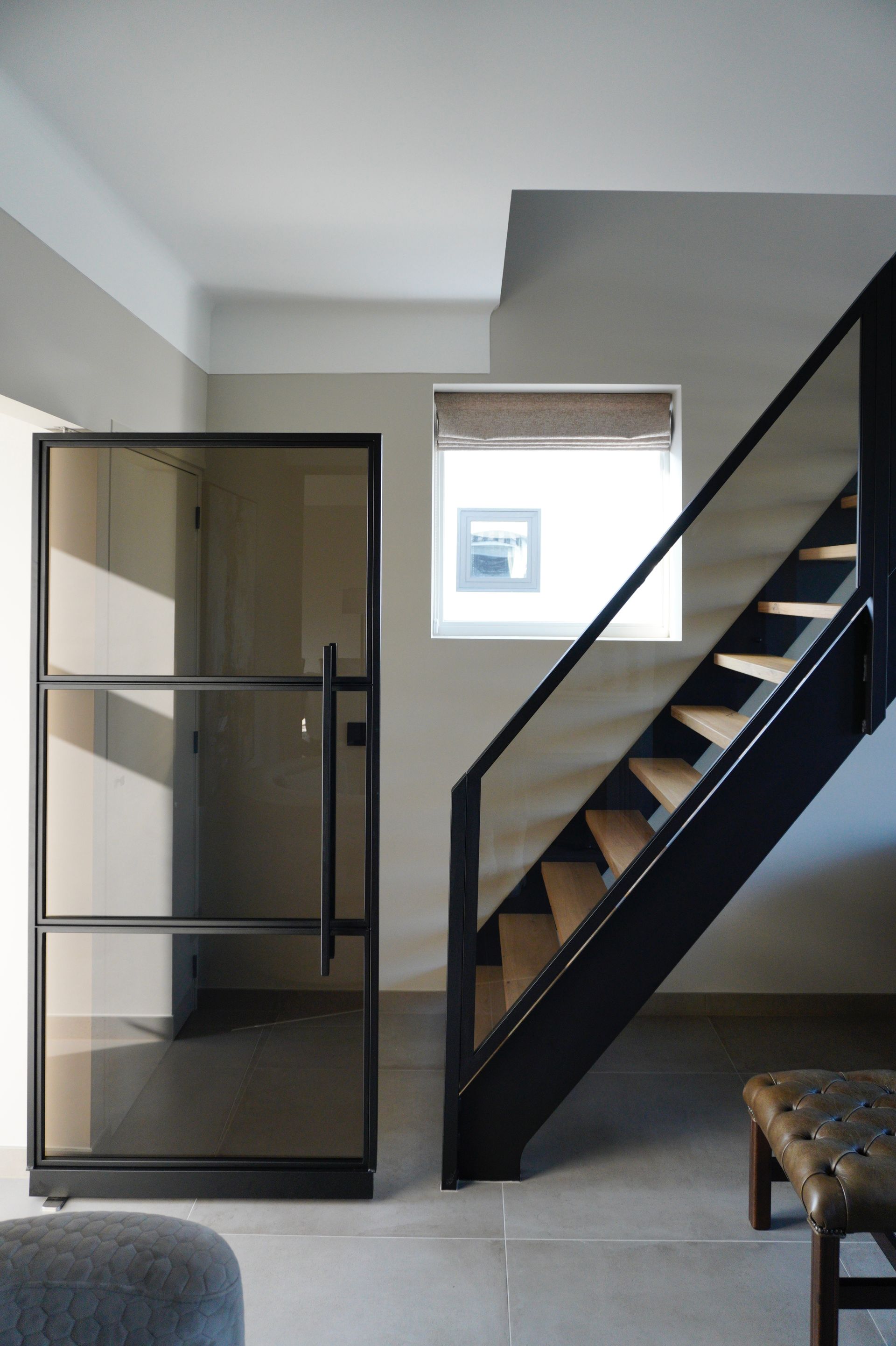 Modern interieur met een zwarte glazen deur en trap, beige muren en houten treden.