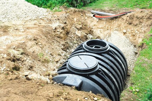 A large black septic tank is sitting in the middle of a dirt field.