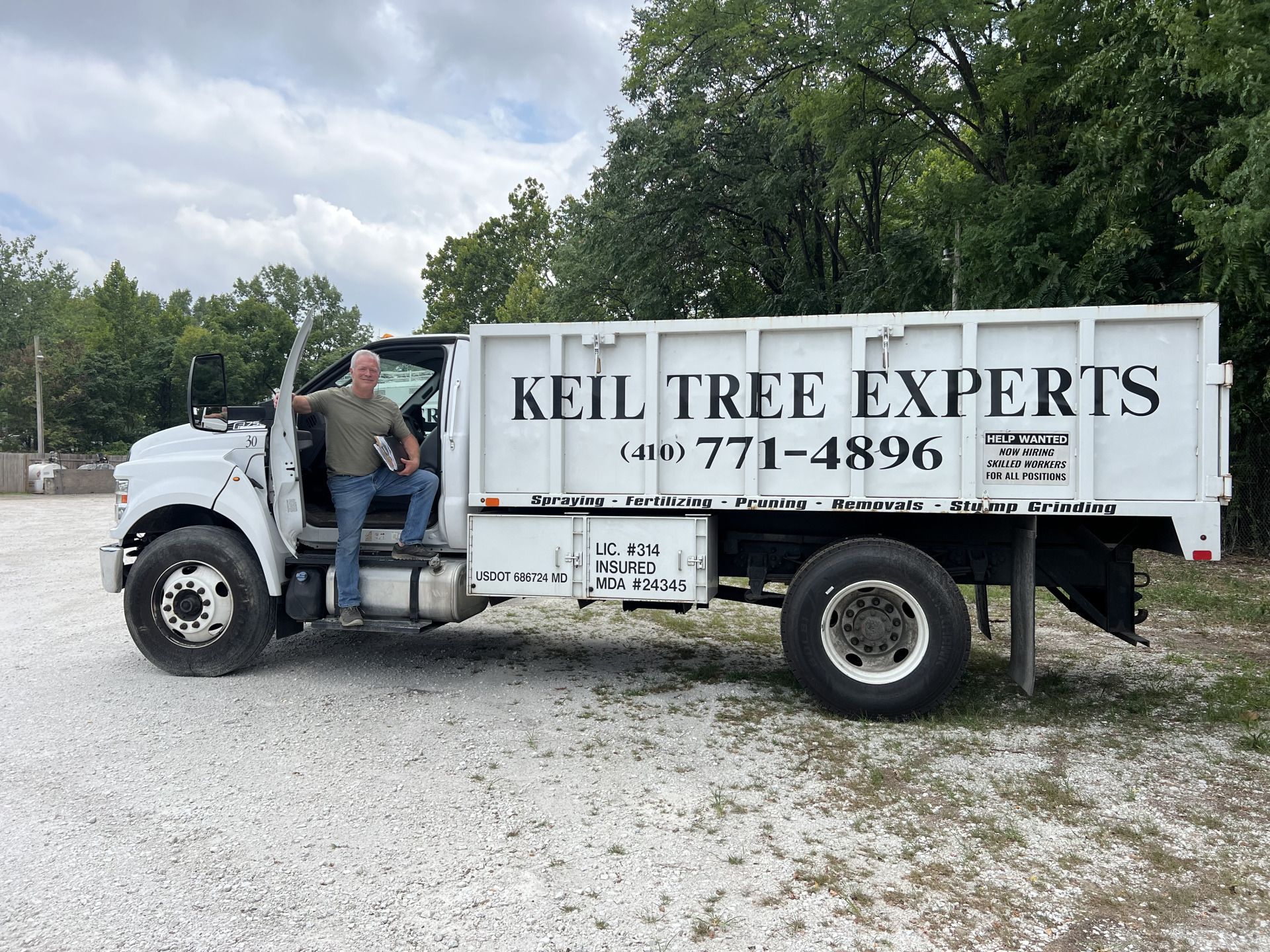 Worker in green jacket spraying around a tree beside a white service truck on a grassy lawn