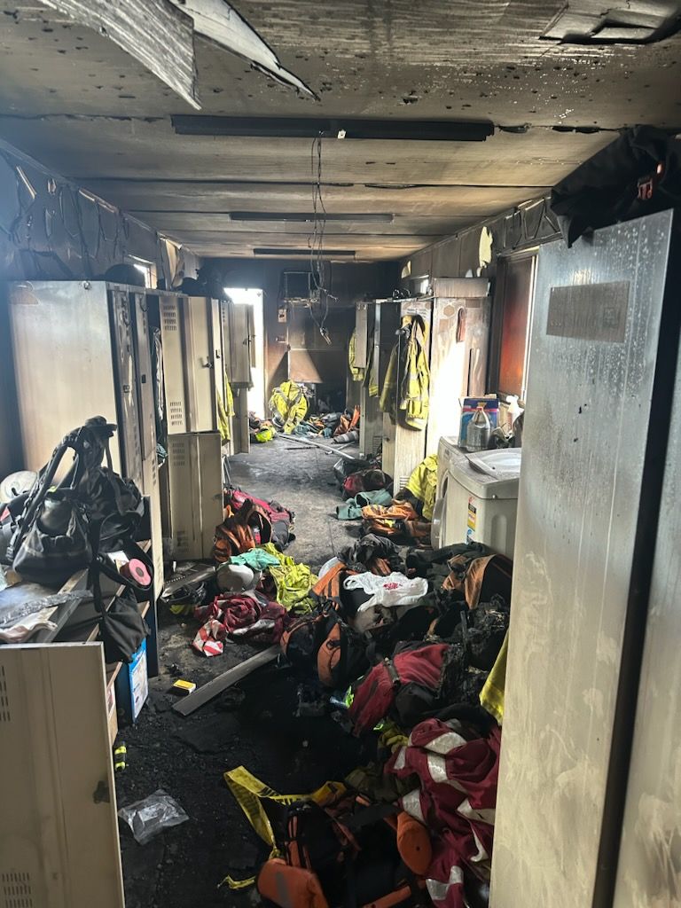 A room damaged from fire filled with lots of clothes and lockers.