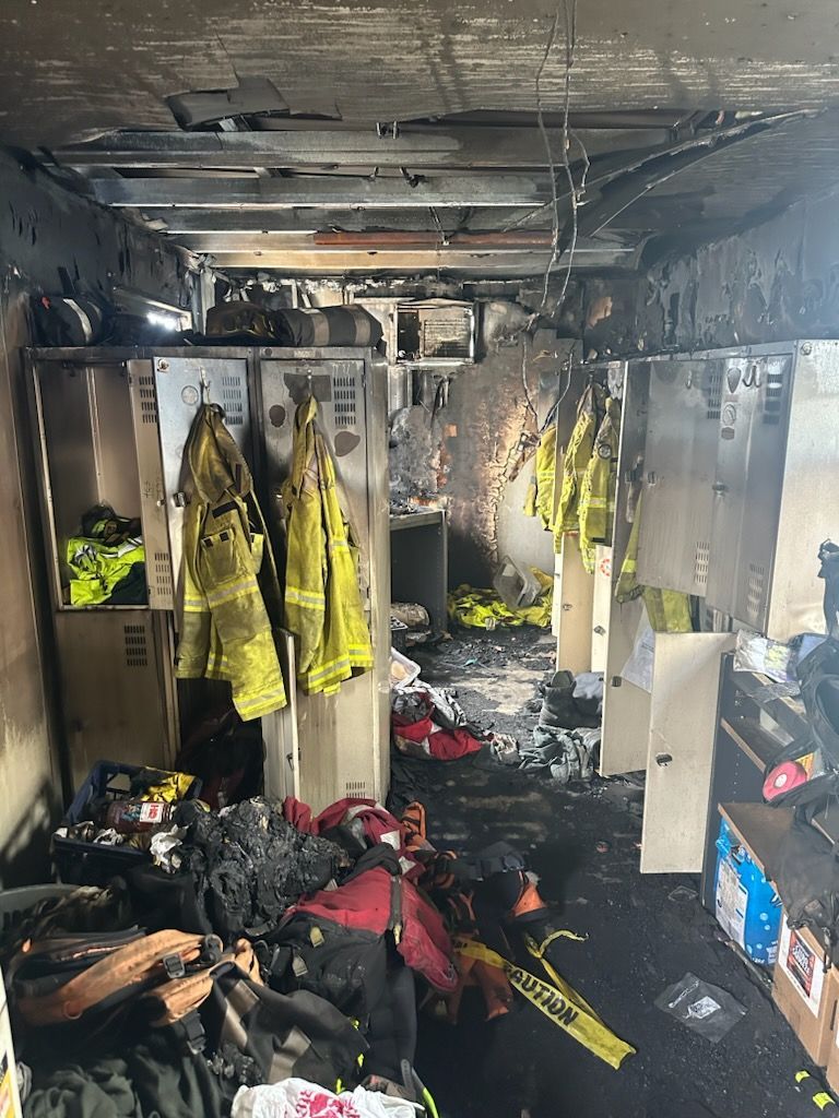 A fire damaged locker room with a lot of clothes hanging on the lockers.