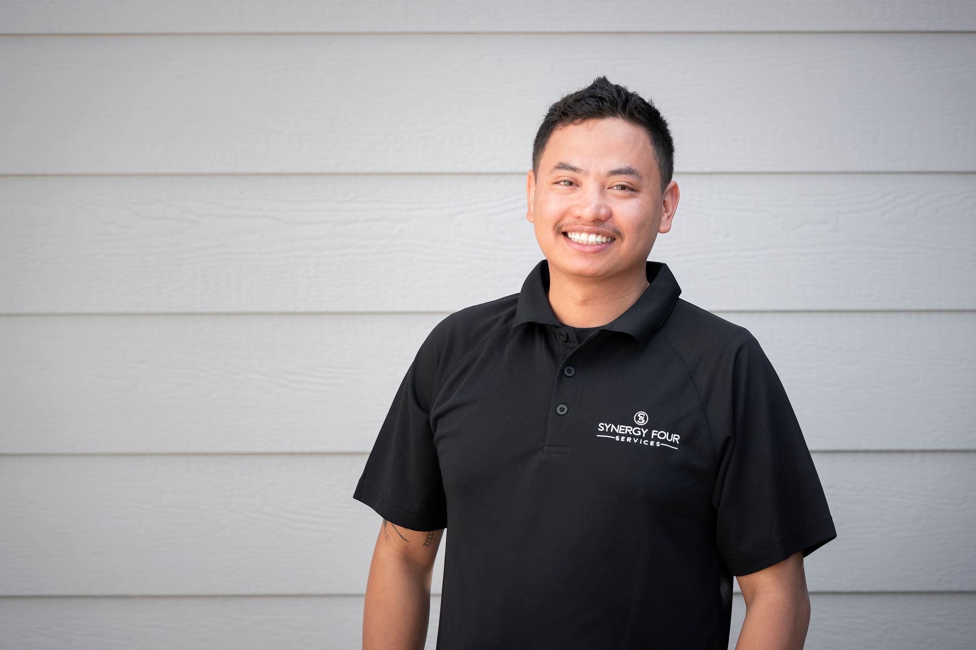 A man in a black shirt is standing in front of a white wall.