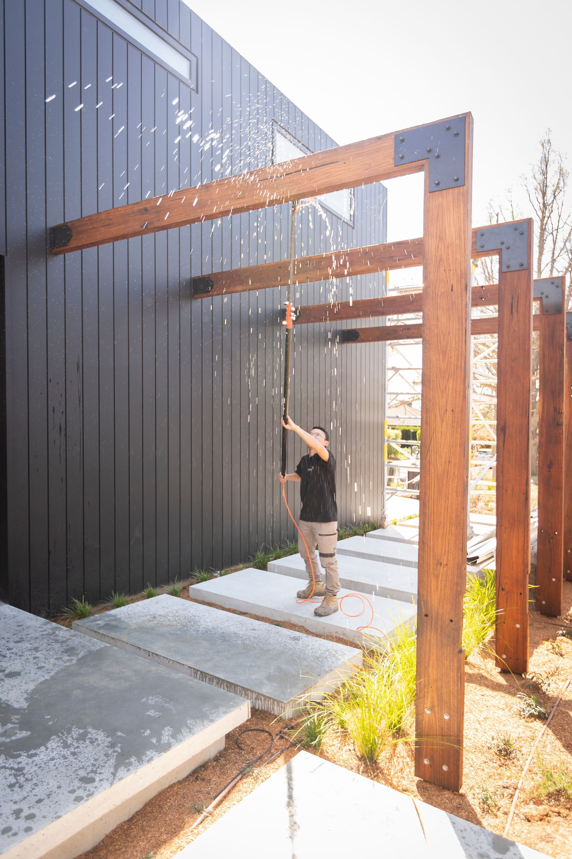 A man is spraying water from a hose outside of a building.