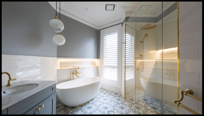 Modern bathroom with a freestanding bathtub, glass shower, patterned floor tiles, and gold fixtures.