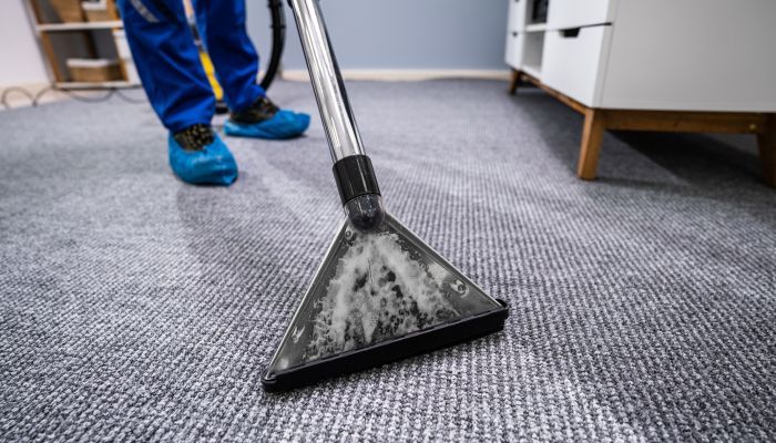 A person is cleaning a carpet with a vacuum cleaner.