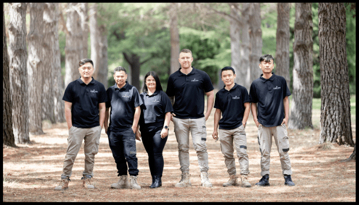 Team of Synergy Four Services staff standing together outdoors in a forested area, wearing matching uniforms.