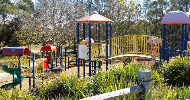 A colorful playground in a park with a wooden fence in the foreground.