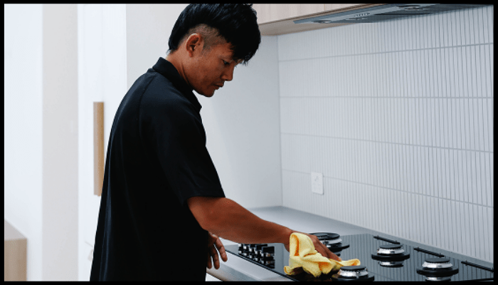 A man is cleaning a stove top in a kitchen.