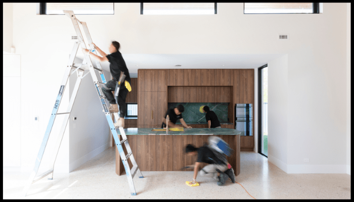Team of professional cleaners working in a modern kitchen, with one person on a ladder and others cleaning surfaces and floors.