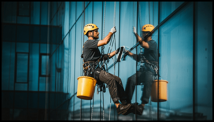 A man is cleaning a building with buckets on a rope.