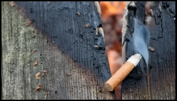 Lit cigarette smoldering on a wooden surface, causing a fire hazard