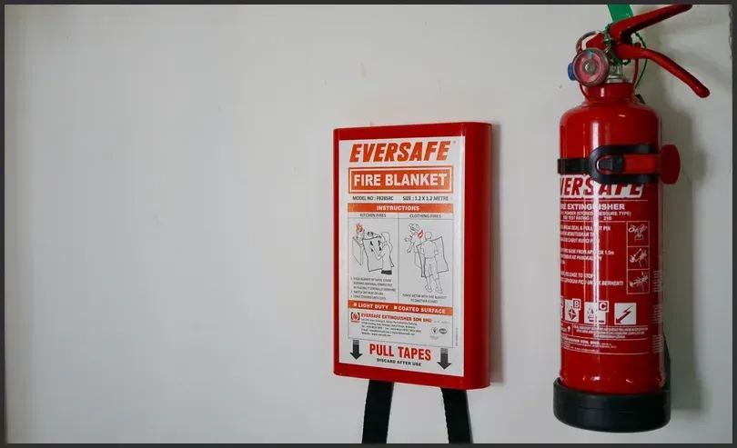 Red fire extinguisher and mounted 'Eversafe' fire blanket on a white wall, essential for home fire safety.