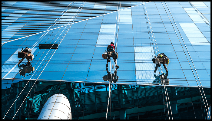 Three professional high-rise window cleaners suspended on ropes working on a modern glass building façade