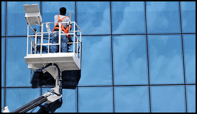 High-rise window cleaner using a boom lift to clean reflective glass panels on a skyscraper