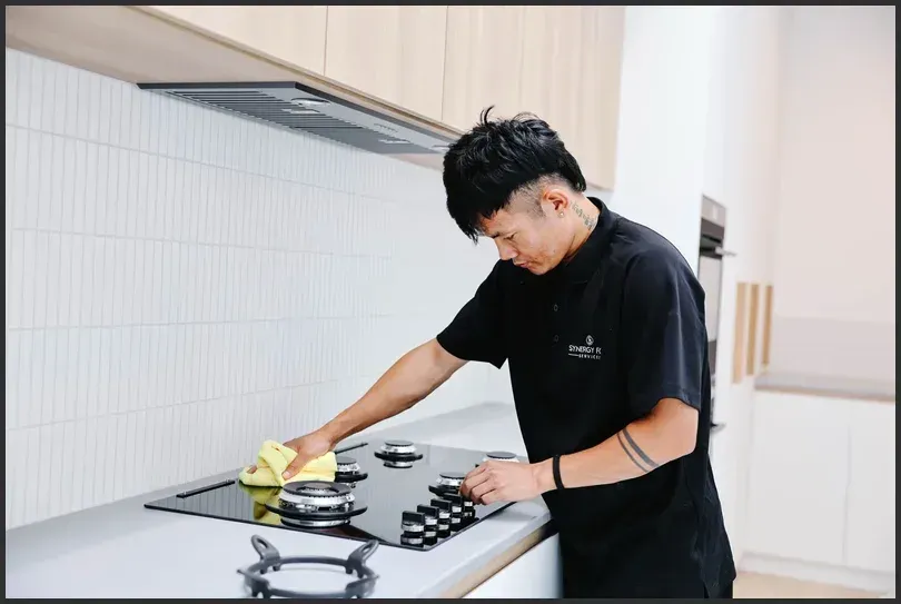A professional cleaner wiping down a kitchen stove to remove grease and stains as part of end-of-lease cleaning.