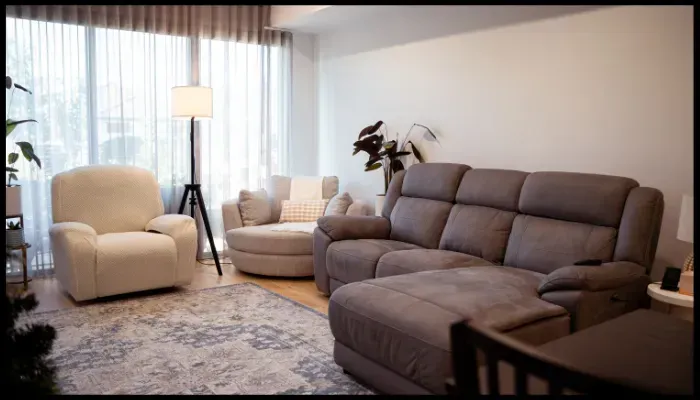 A clean and modern living room with a large sofa, armchair, and natural lighting.
