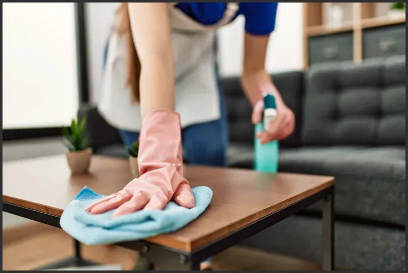 Professional cleaner wiping a wooden table with a cloth and cleaning spray in a living room.