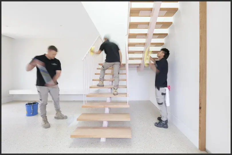 Team cleaning modern wooden staircase in a bright, spacious home.