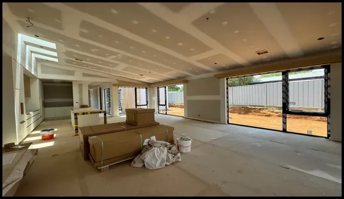 unfinished interior of a modern home under construction, with drywall installed and construction materials scattered on the floor.