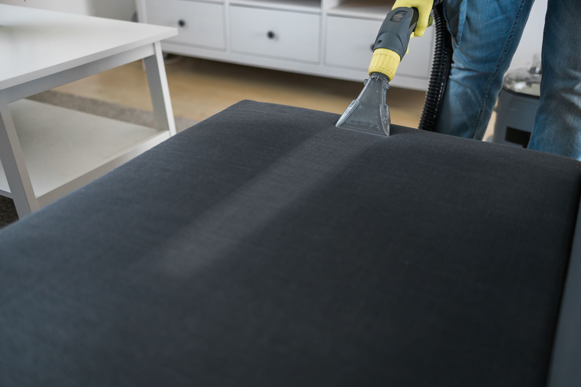 A person wearing blue gloves is cleaning a bed with a vacuum cleaner.