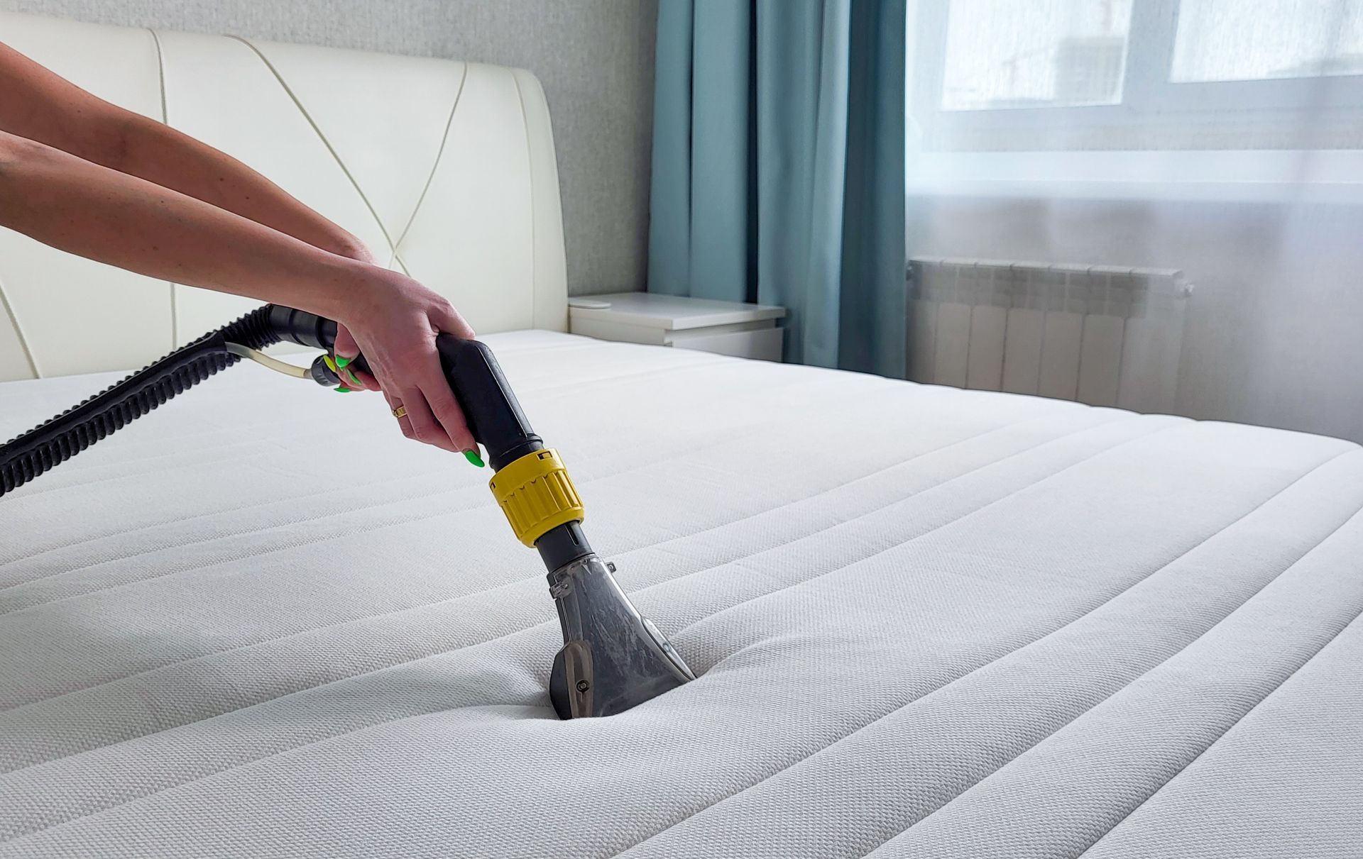 A person is cleaning a mattress with a vacuum cleaner.