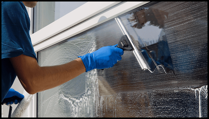 Close-up of a professional window cleaner using a squeegee on soapy commercial glass window