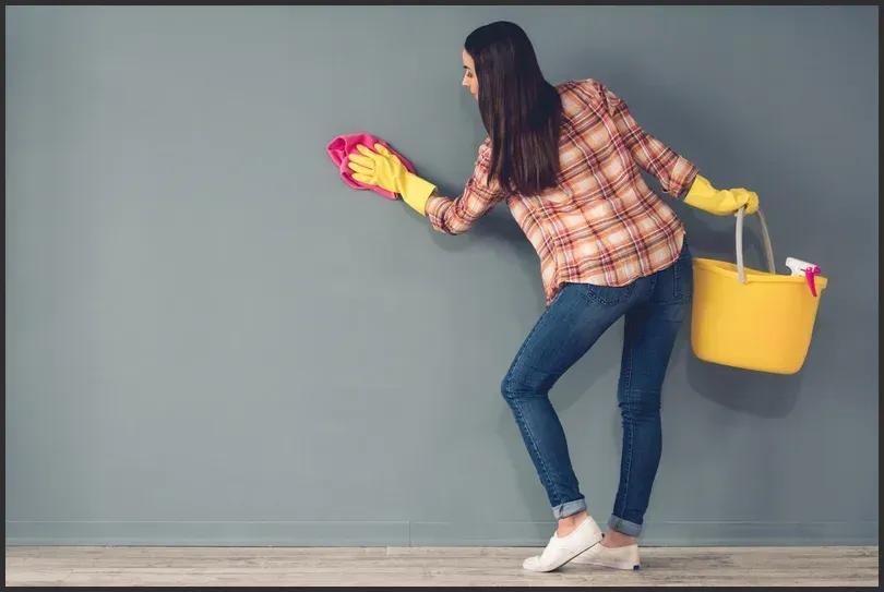 A woman cleaning a wall with a cloth and holding a bucket, ensuring the rental property meets end-of-lease cleaning requirements.
