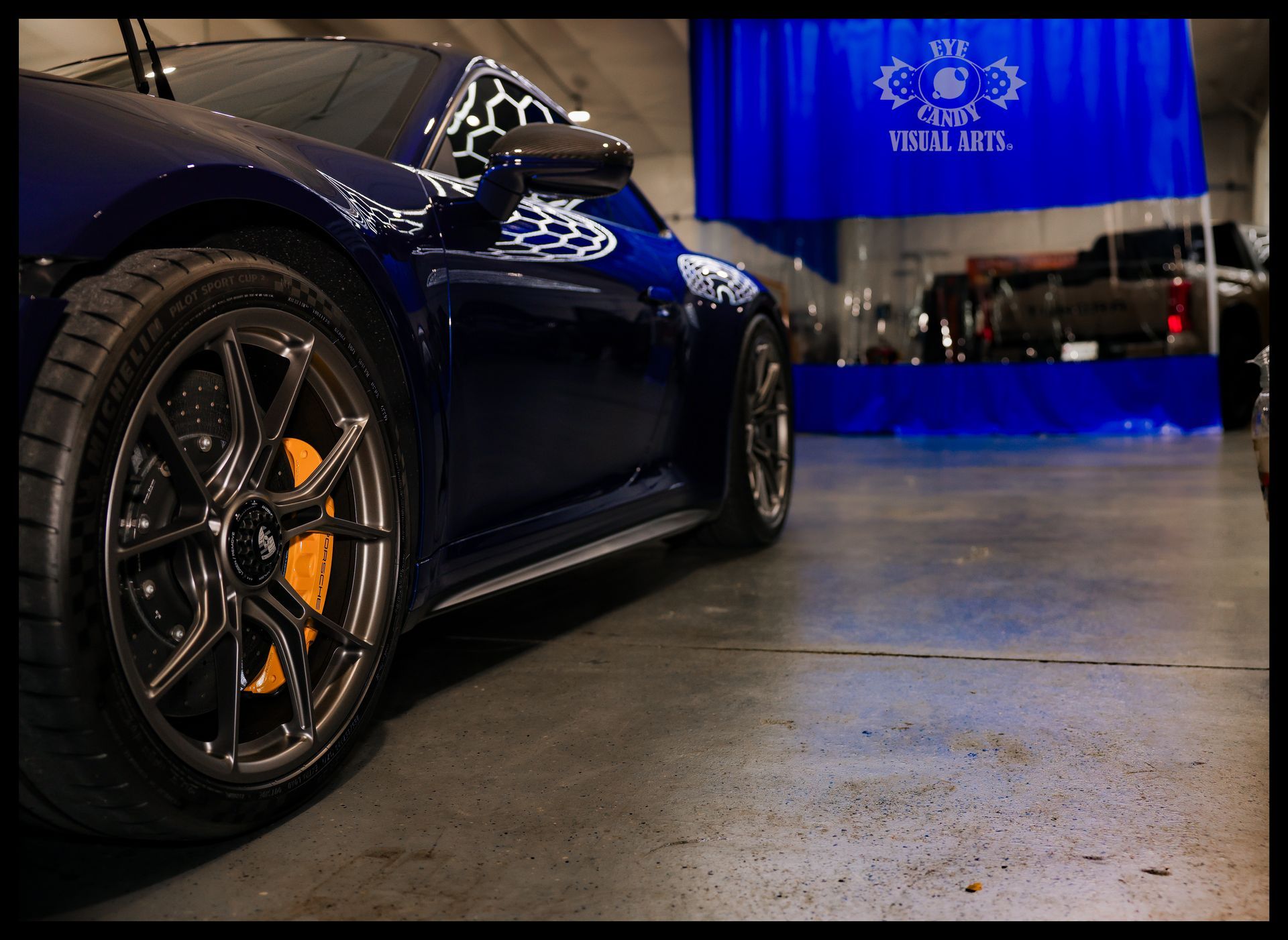 Blue sports car on display in a showroom with a blue Rolls-Royce banner in the background