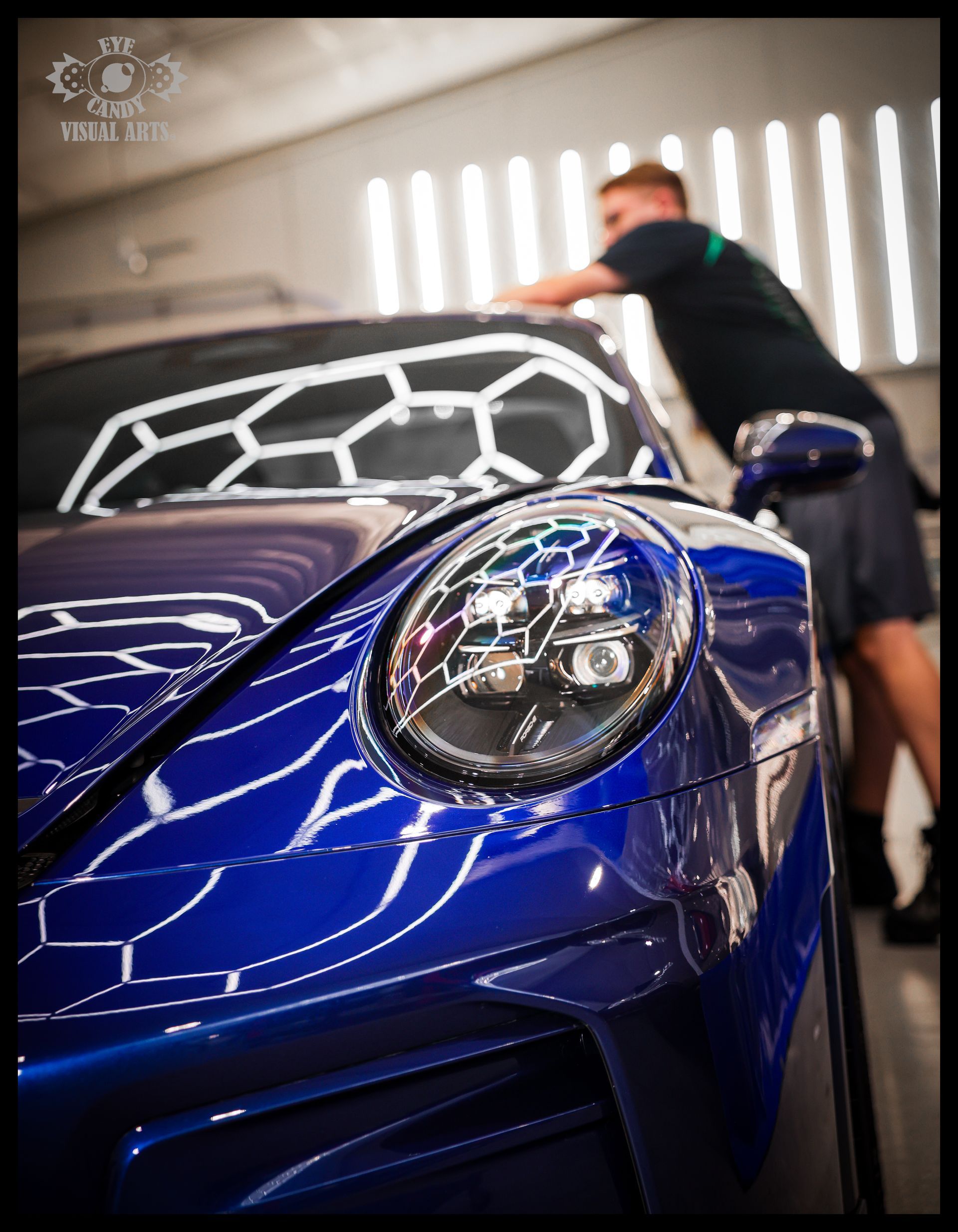 Blue sports car being polished in a bright garage, with a person leaning over it.