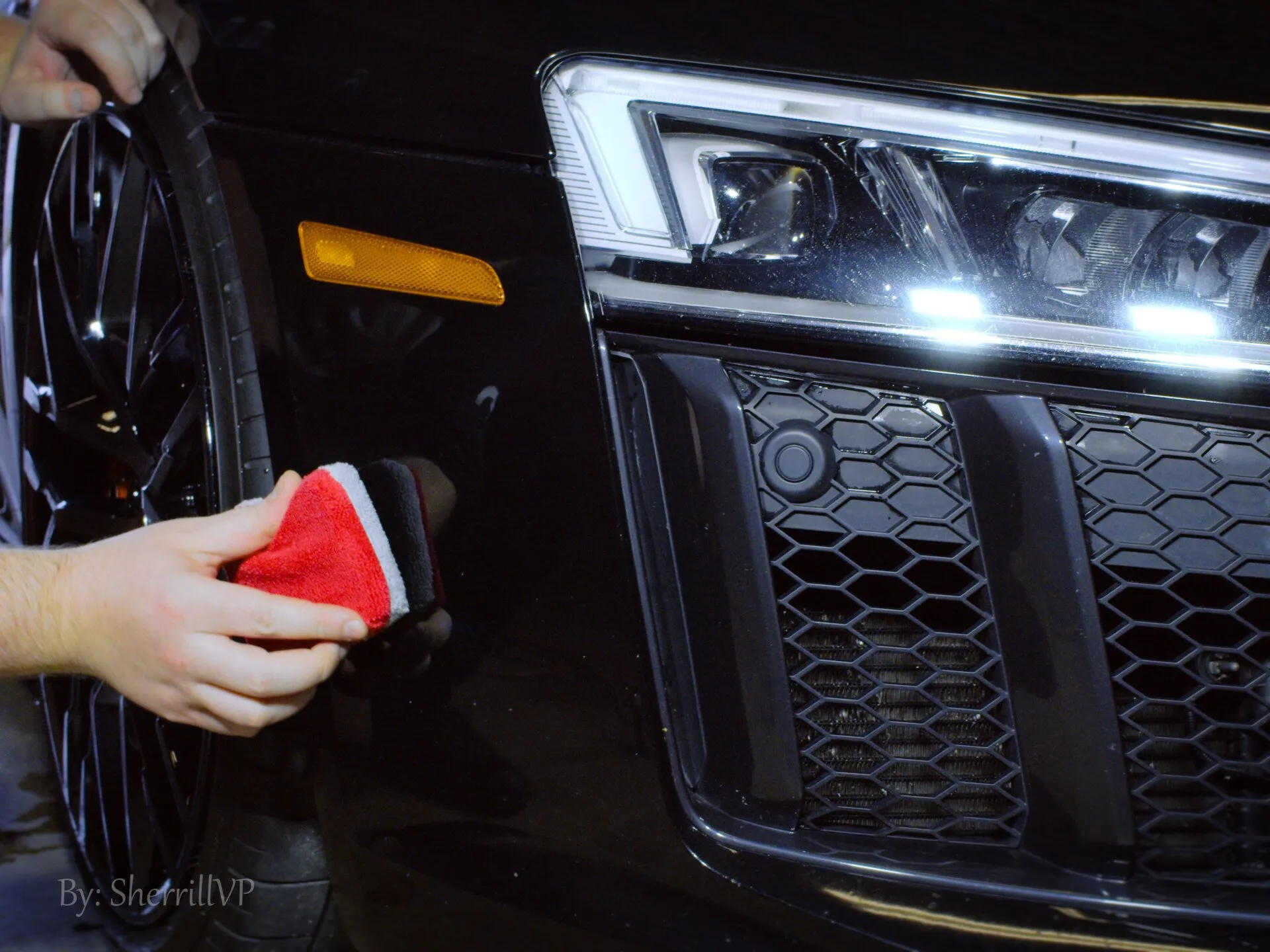 Hand washing a black car’s front grille with a red sponge
