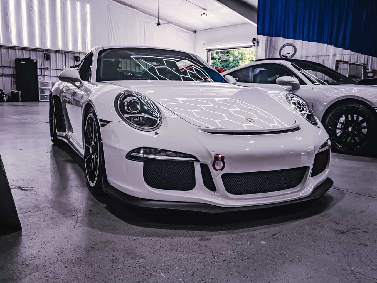 White sports car displayed indoors at a car show, front view with black accents