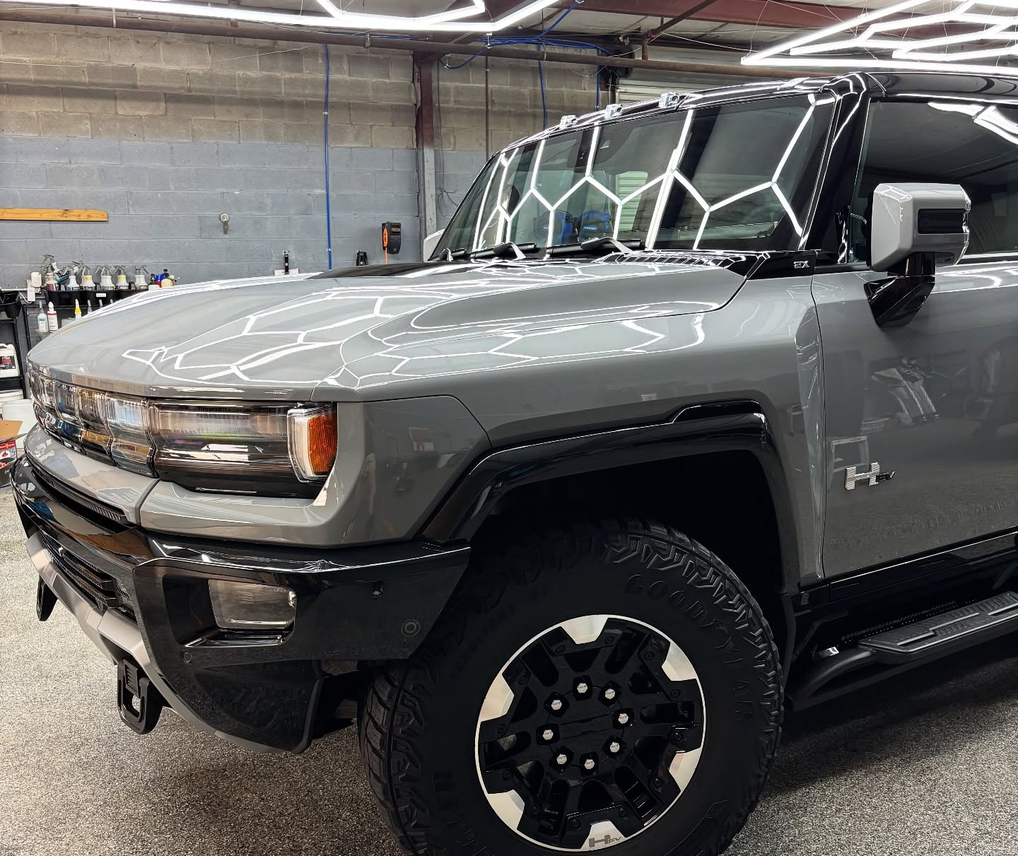 Gray Hummer EV parked in a garage, black accents, honeycomb windshield, black wheels.
