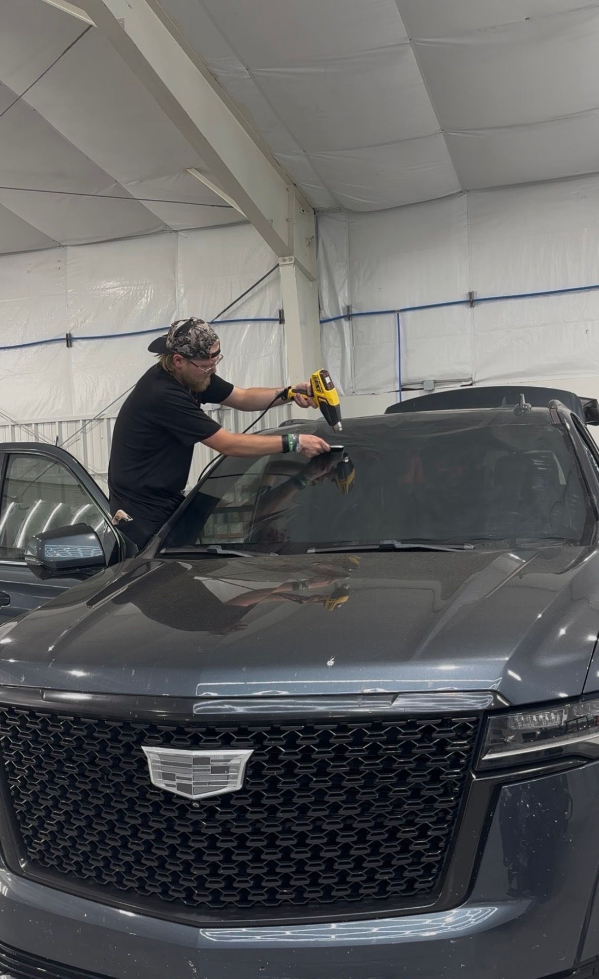A man is installing window tinting on a car in a garage.