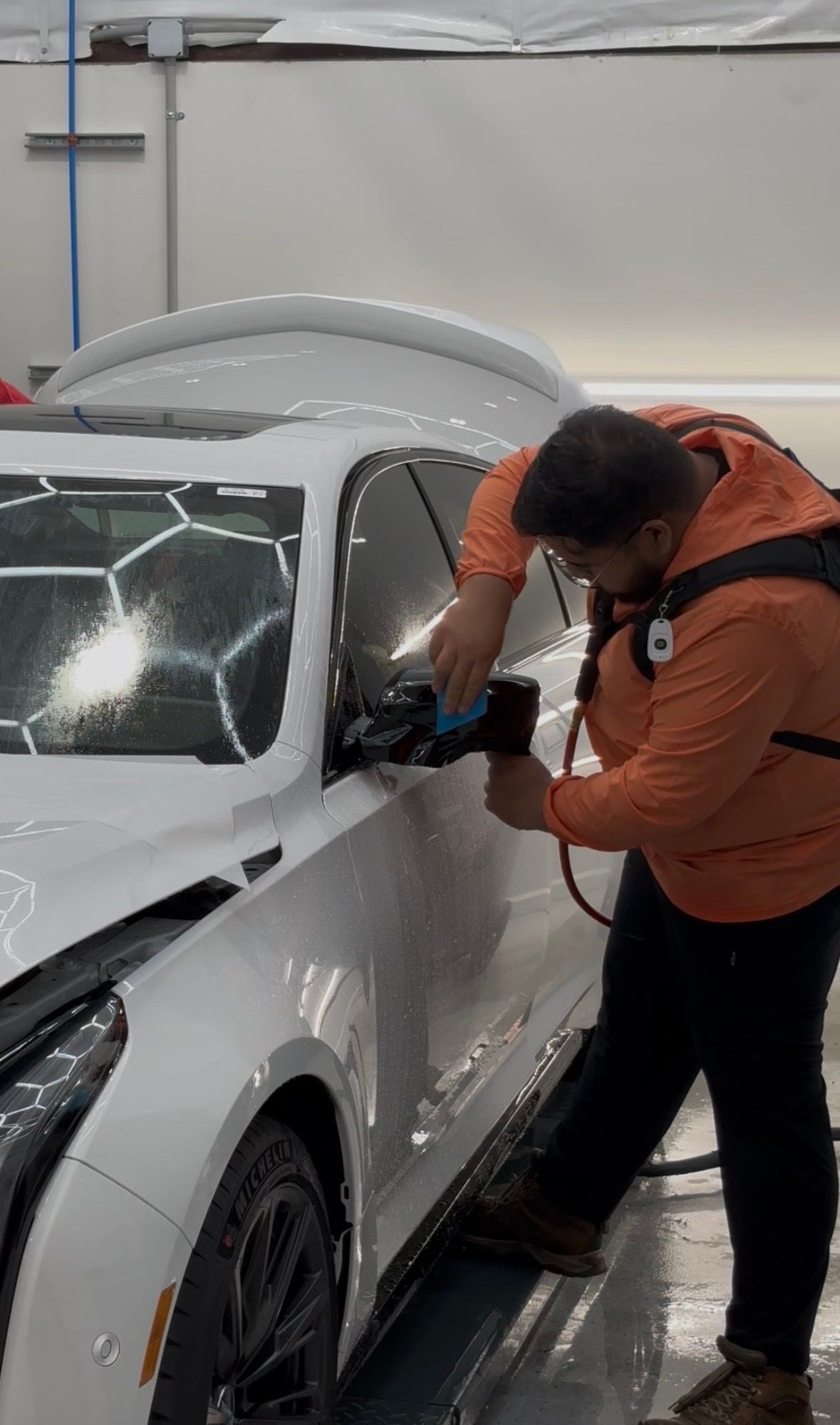 Person polishing the side of a white sports car in an indoor auto body shop