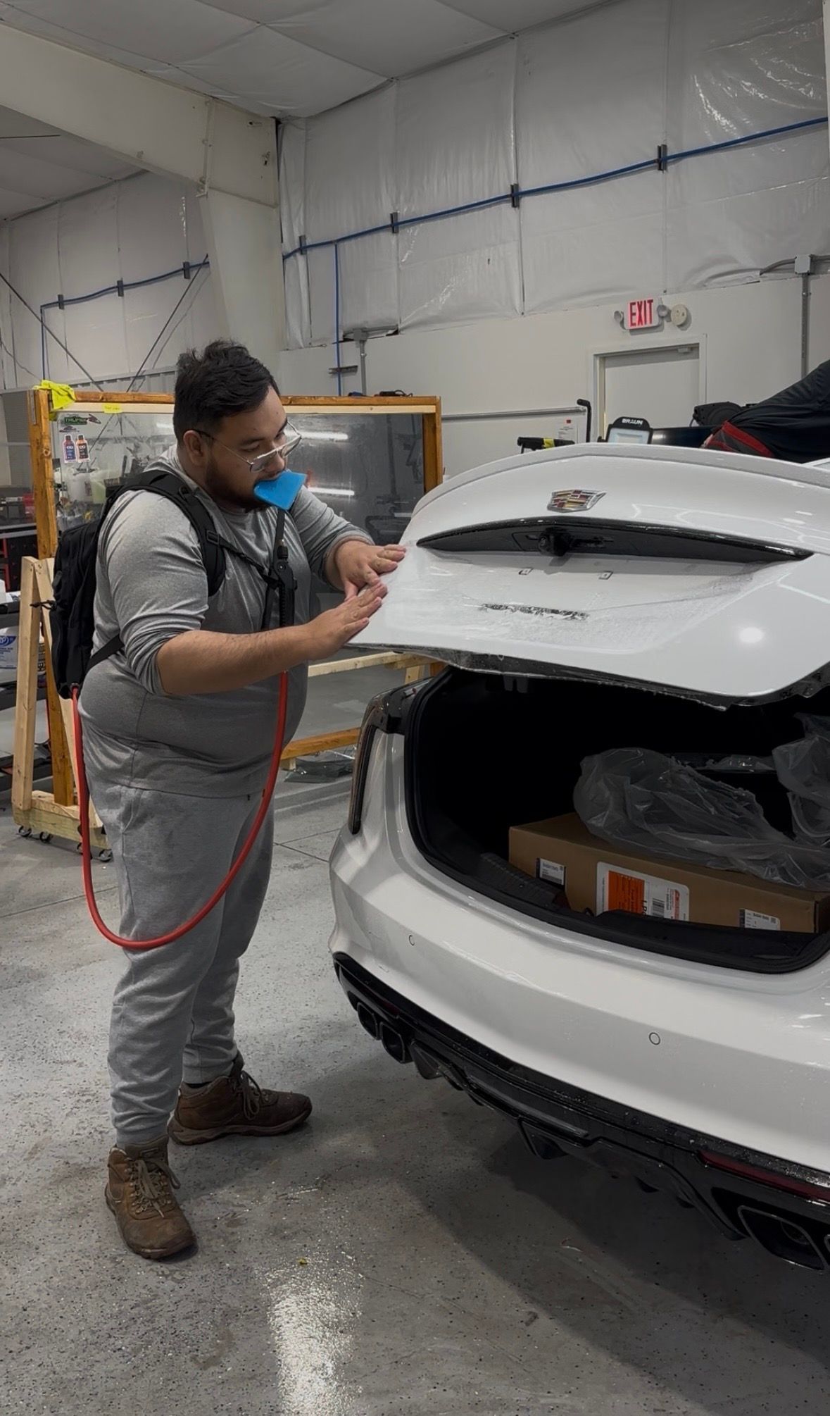 Technician inspecting the open hatch of a white SUV in an auto body shop
