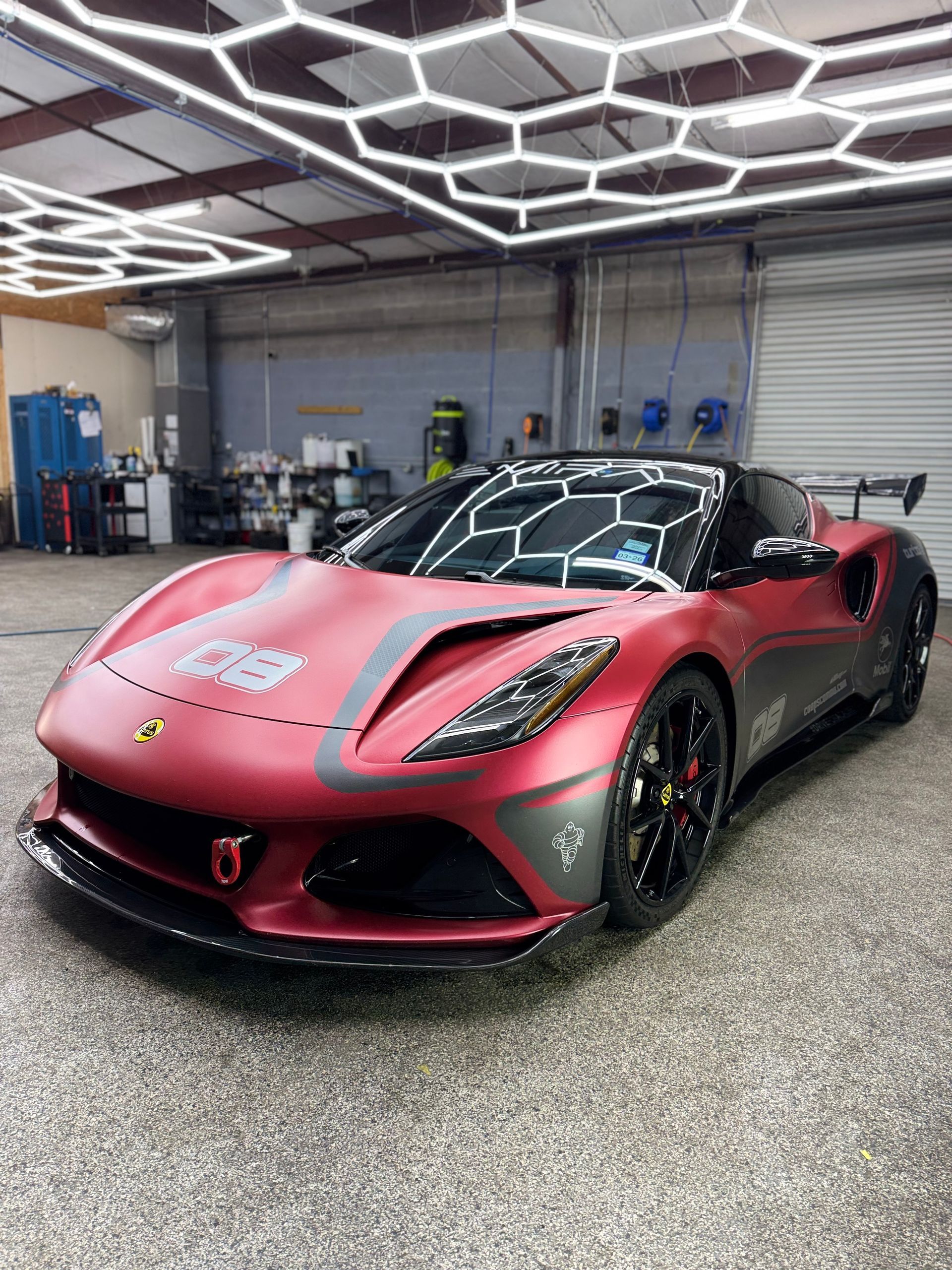 Red sports car in a garage with honeycomb-shaped ceiling lights.