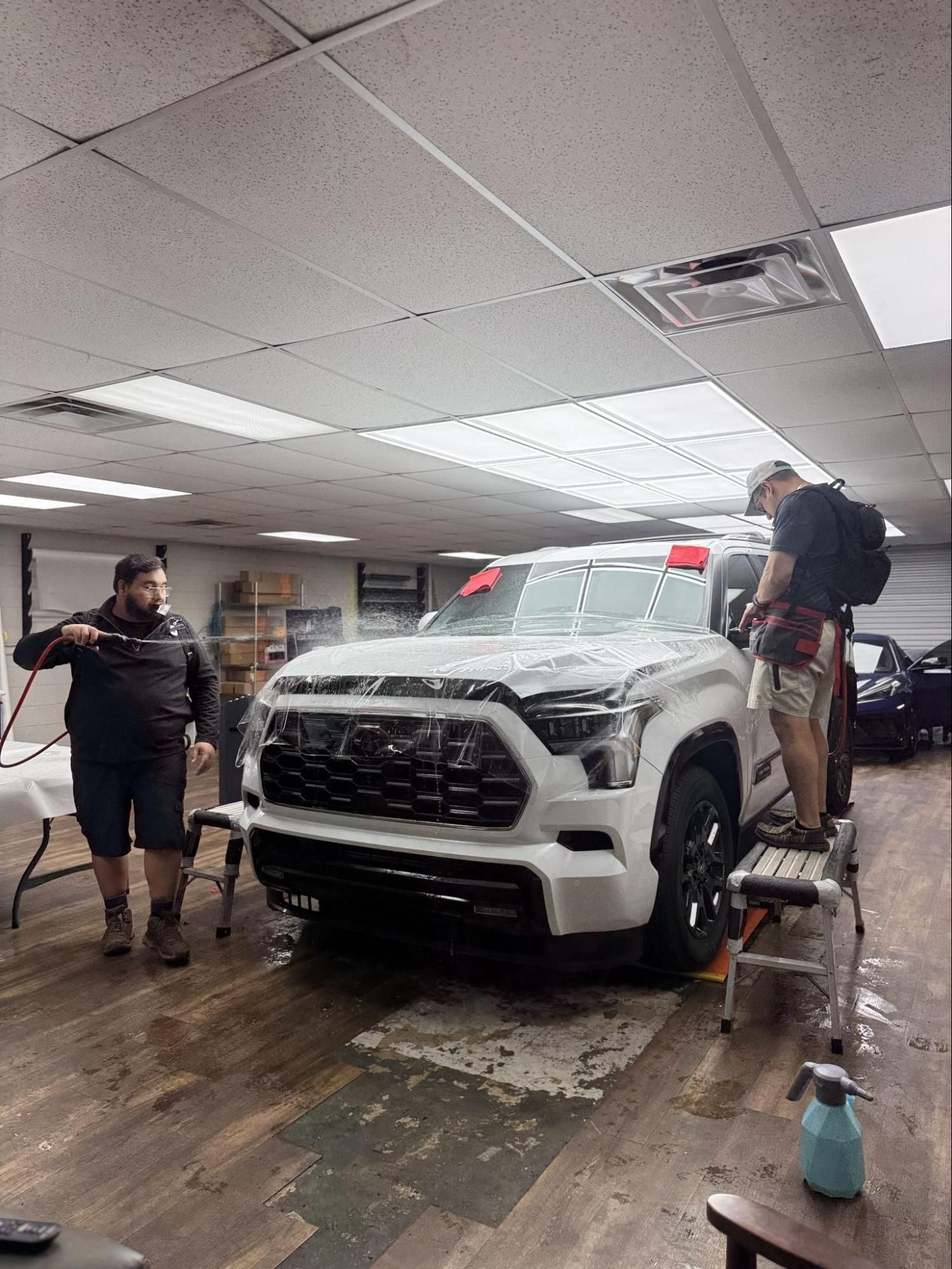 SUV being washed indoors by two people in a car wash bay