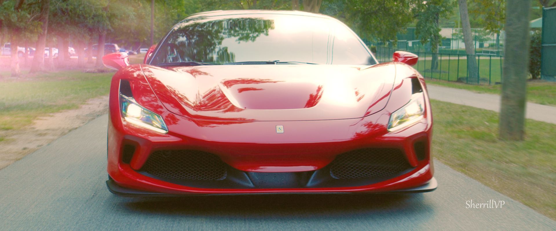 Red Ferrari sports car driving on a paved road with trees on either side.