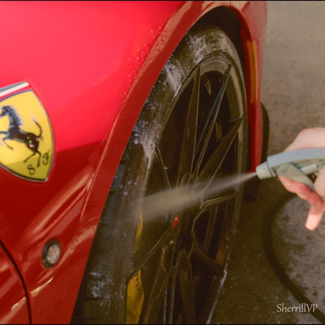 A person spraying water on a red Ferrari's tire, next to the Ferrari emblem.
