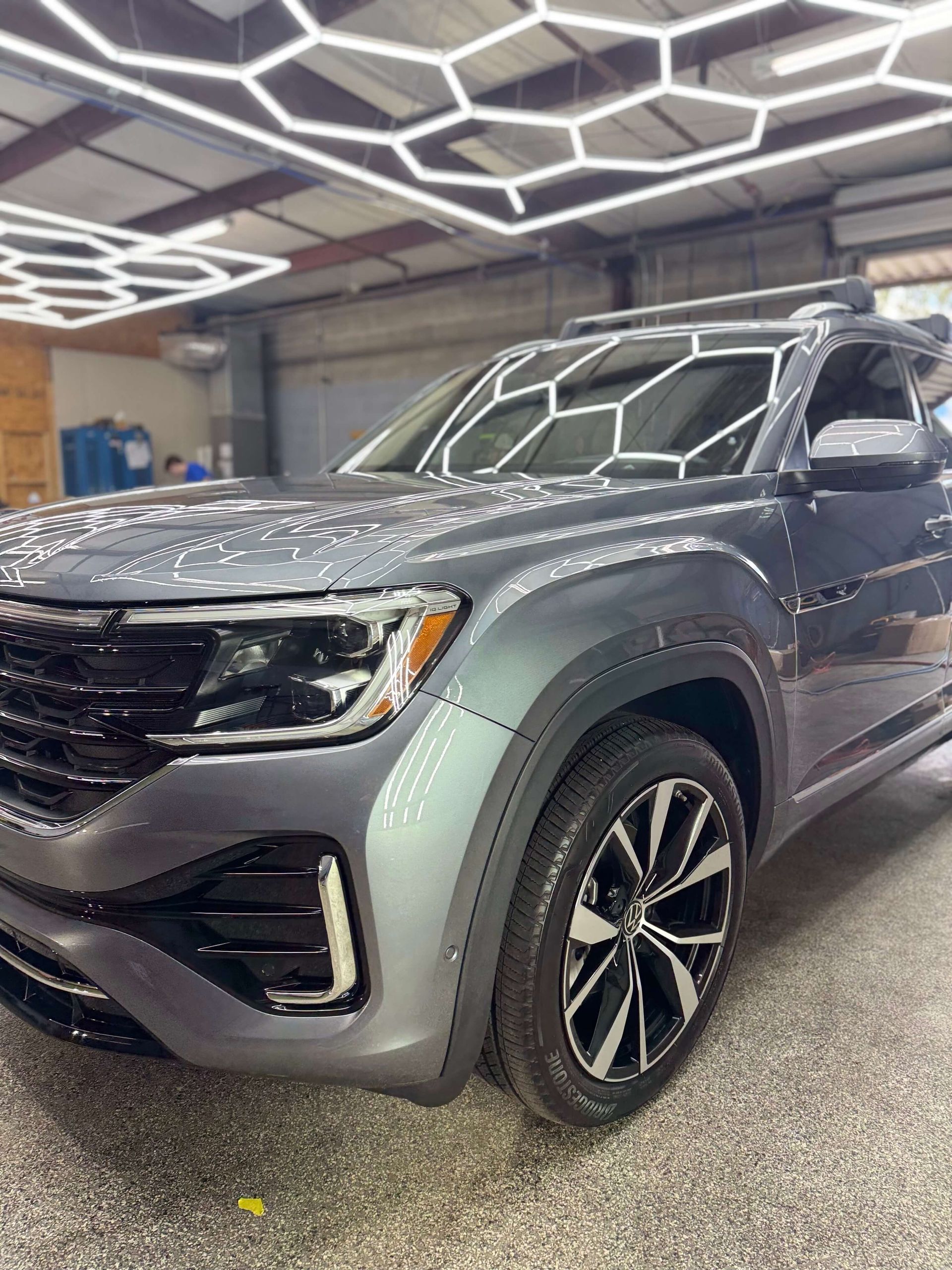 Gray Volkswagen Atlas SUV in a garage, reflecting hexagonal ceiling lights.