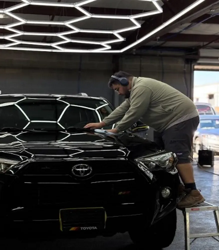 Person polishing a black Toyota SUV in a garage under hexagonal ceiling lights