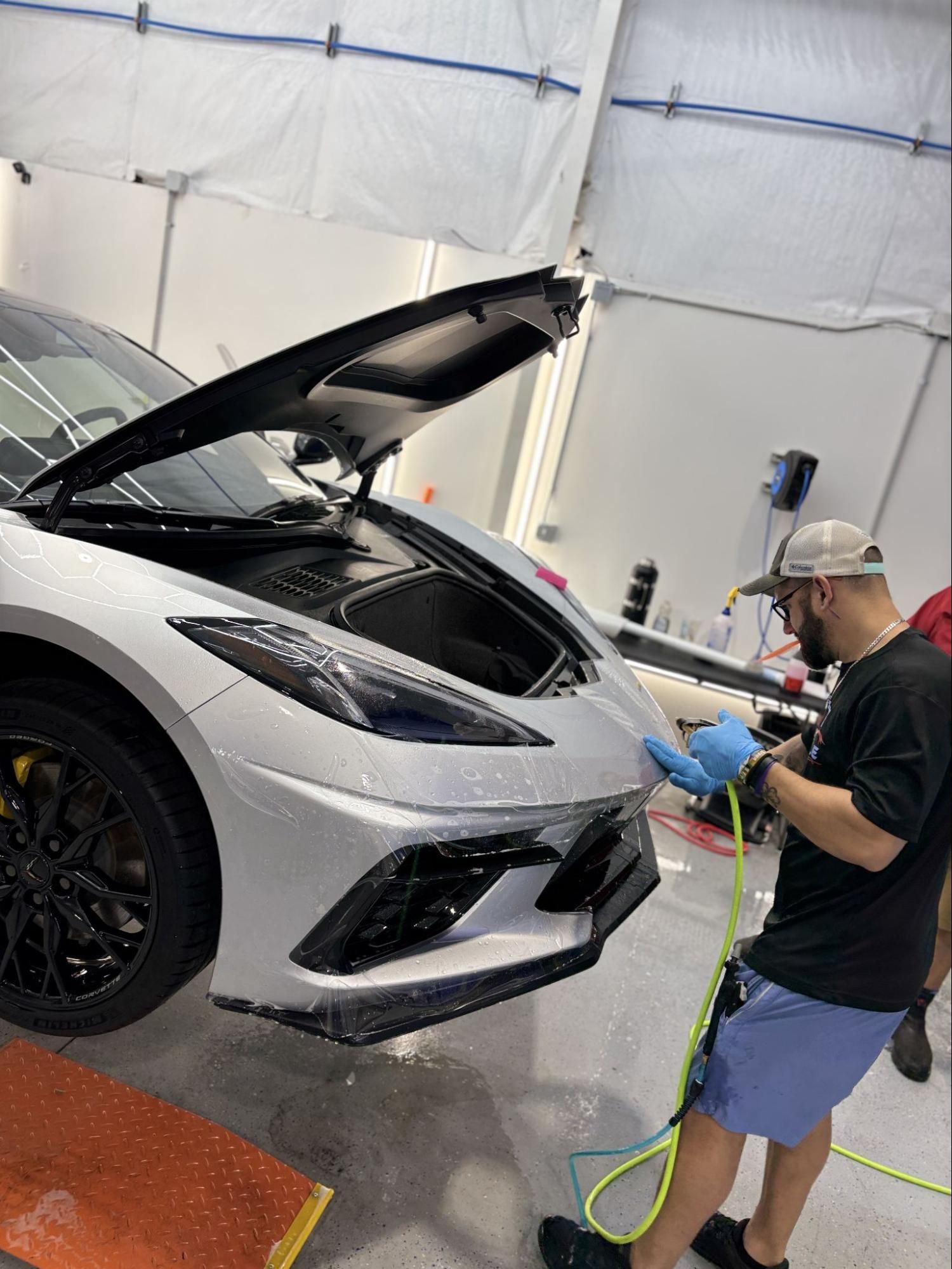 White sports car being washed in a garage by a person with a pressure washer