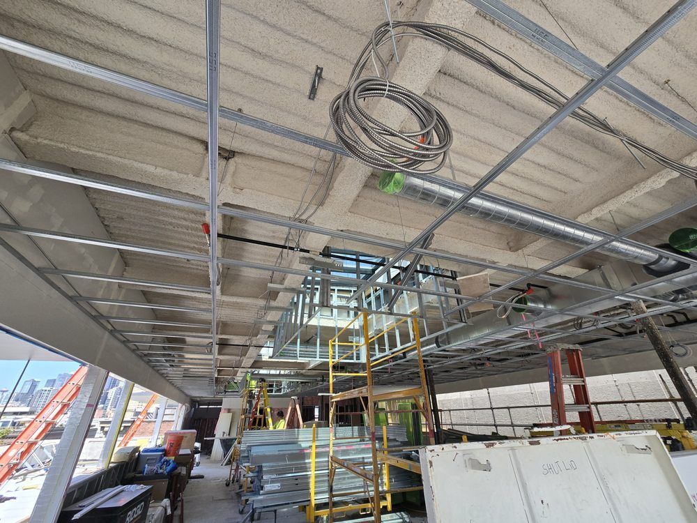Interior of a building under construction with scaffolding, exposed ceiling beams, and hanging electrical cables.