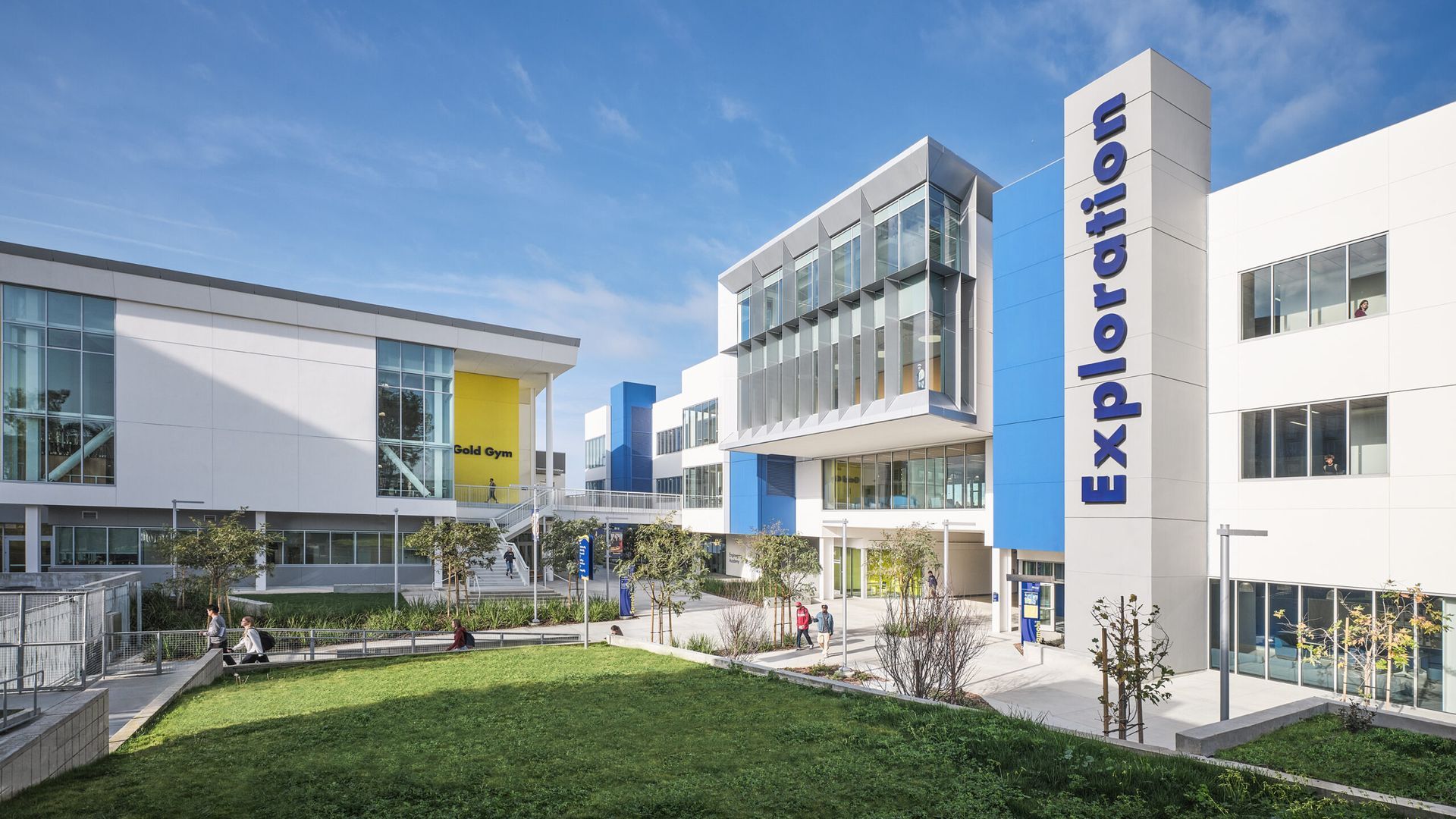 Modern school campus with white buildings, glass windows, blue accents, a green lawn, and a sign reading
