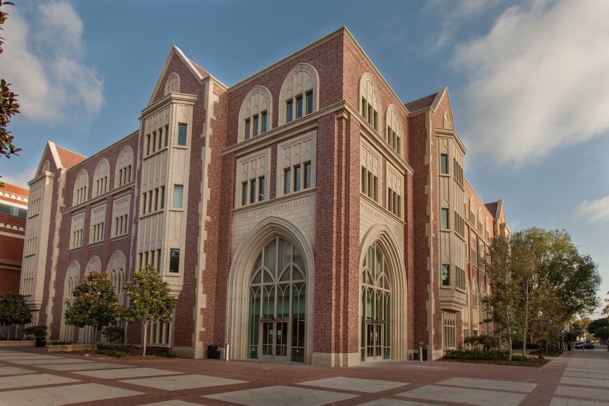 A multi-story collegiate gothic style building made of red brick and white stone, set on a sunny day with trees nearby.